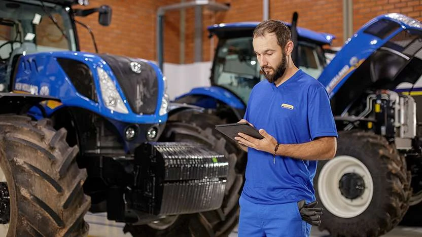 Técnico em uniforme azul trabalhando entre tratores New Holland