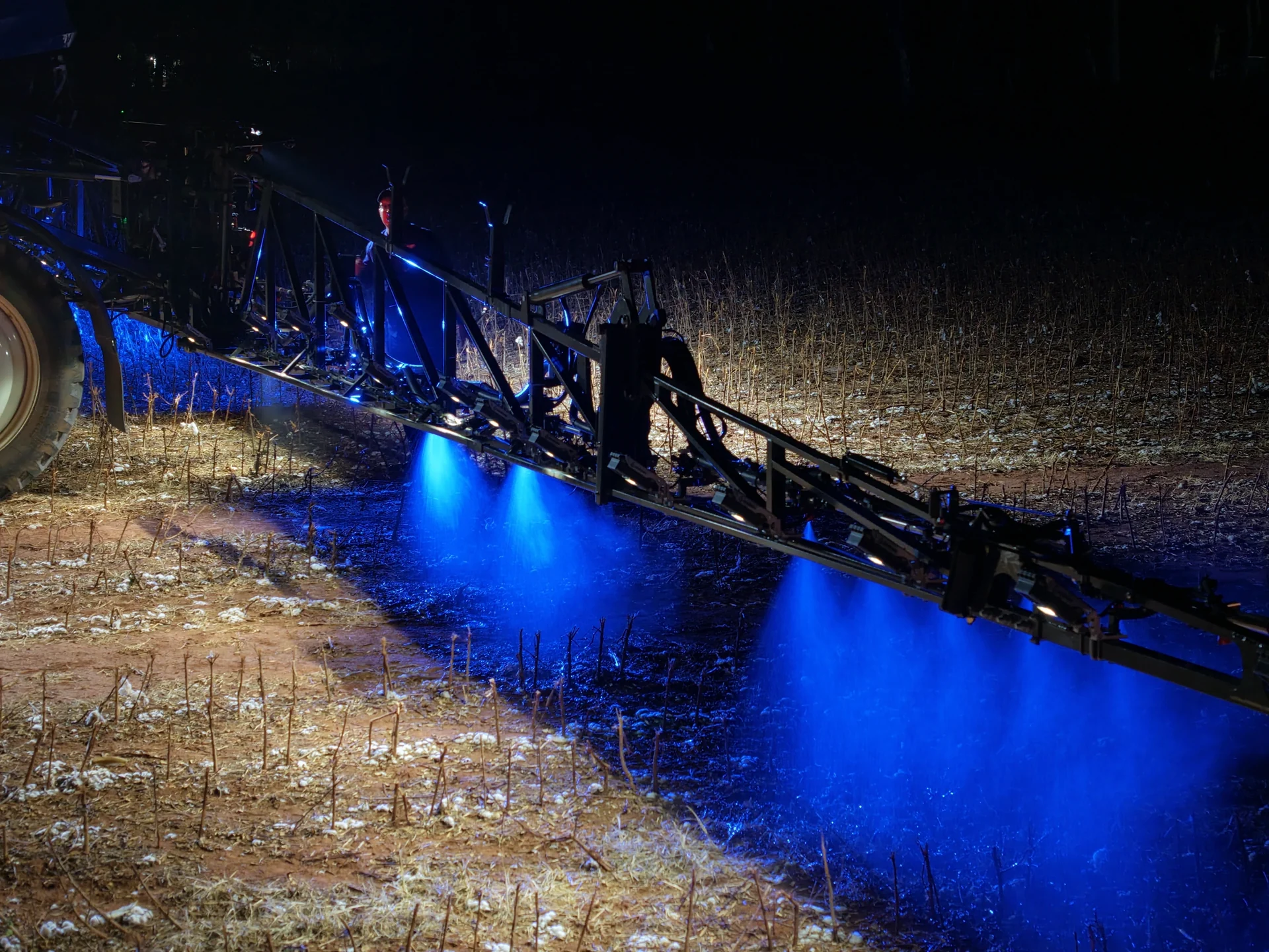 Fotografia real da barra New Holland em aplicação noturna, com iluminação azul sobre os jatos e a palhada do algodão